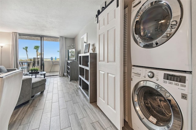 laundry area featuring a barn door, a textured ceiling, light hardwood / wood-style flooring, and stacked washer and clothes dryer