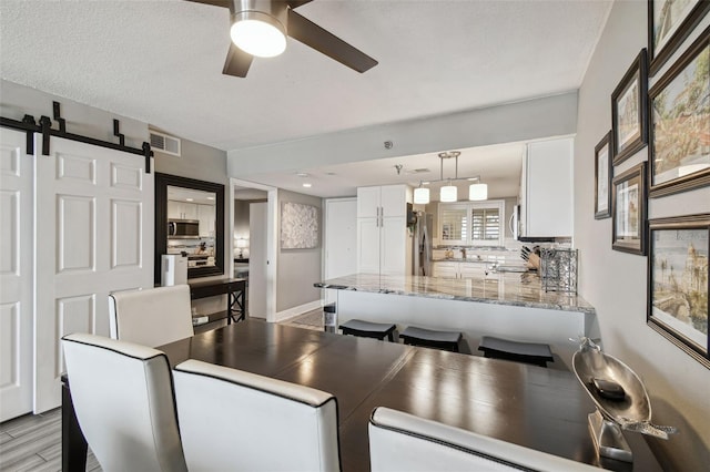 dining space featuring a barn door, ceiling fan, and a textured ceiling