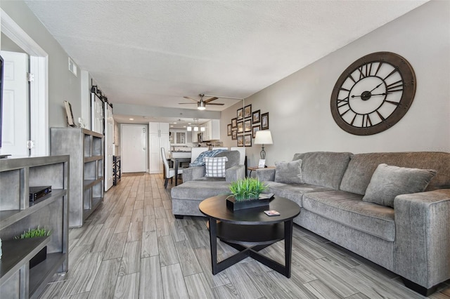 living room with ceiling fan, light wood-type flooring, and a textured ceiling