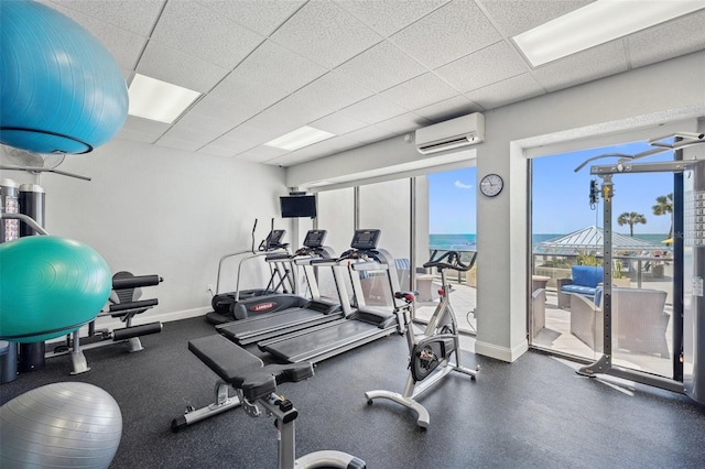 exercise room featuring a water view, a wall mounted AC, and a paneled ceiling