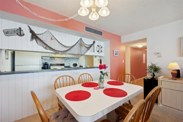 dining room featuring a textured ceiling, carpet floors, and an inviting chandelier