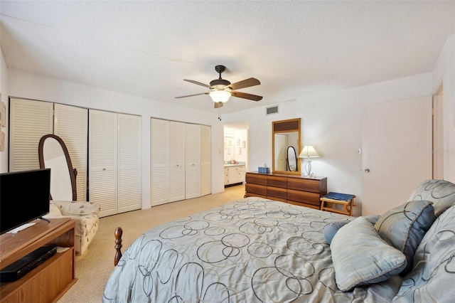 carpeted bedroom featuring multiple closets, a textured ceiling, ceiling fan, and ensuite bathroom