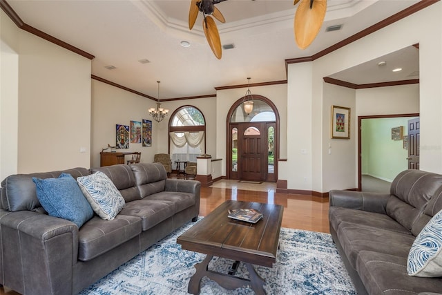 living room with wood-type flooring, ceiling fan with notable chandelier, and crown molding