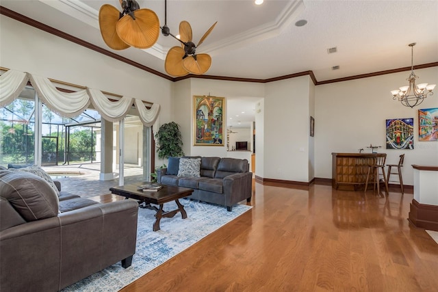 living room featuring hardwood / wood-style floors, a chandelier, a raised ceiling, and crown molding