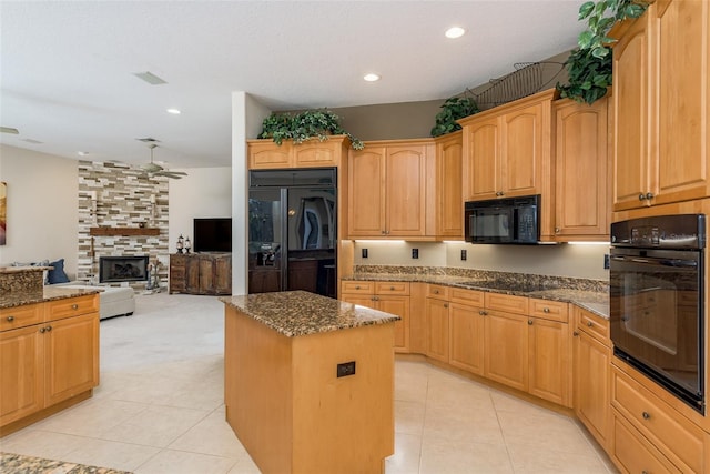 kitchen featuring a stone fireplace, ceiling fan, light tile flooring, black appliances, and a center island