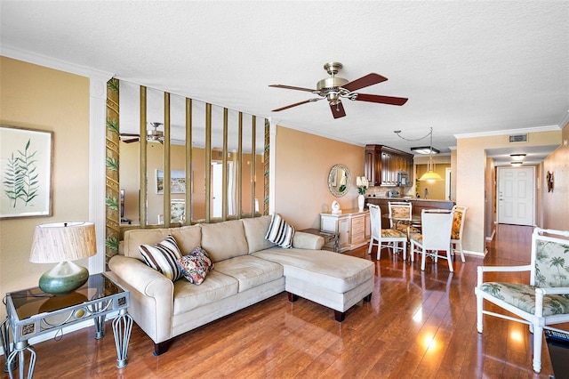 living room with dark hardwood / wood-style floors, ceiling fan, ornamental molding, and a textured ceiling