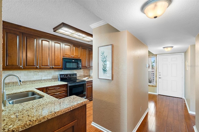 kitchen with sink, tasteful backsplash, light stone counters, dark hardwood / wood-style flooring, and black appliances