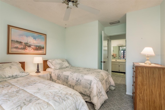 bedroom with ceiling fan, carpet flooring, ensuite bath, and a textured ceiling