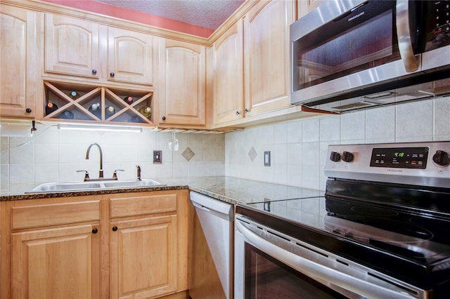 kitchen featuring stainless steel appliances, tasteful backsplash, dark stone counters, light brown cabinetry, and sink