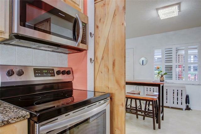 kitchen with appliances with stainless steel finishes, light brown cabinetry, light tile flooring, backsplash, and radiator