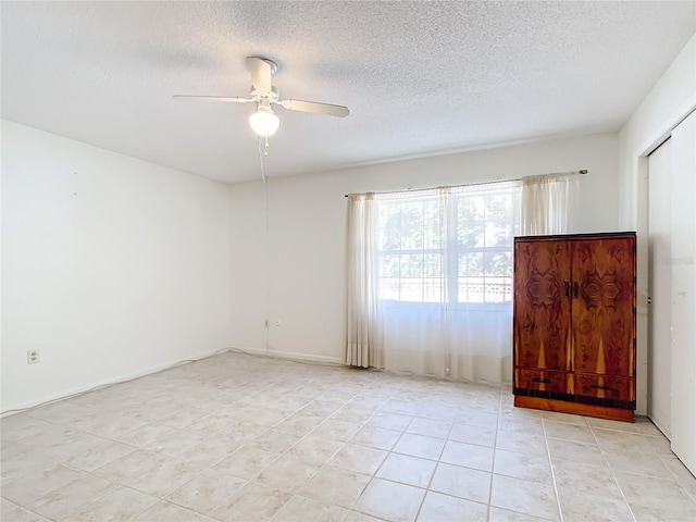 empty room with a textured ceiling, light tile patterned floors, and ceiling fan