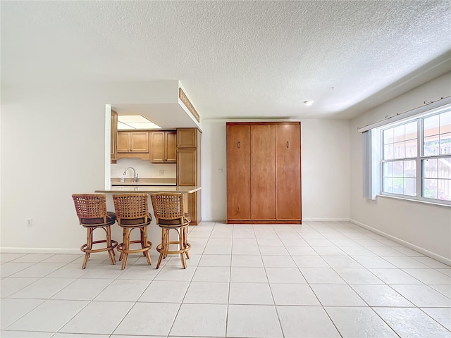 kitchen with kitchen peninsula, a textured ceiling, light tile patterned floors, and a breakfast bar area