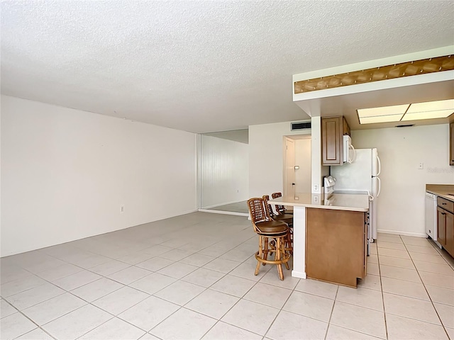 kitchen featuring light tile patterned flooring, a textured ceiling, white appliances, and a breakfast bar area