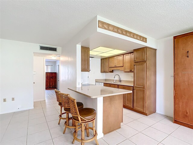 kitchen with a textured ceiling, light tile patterned floors, a breakfast bar, a kitchen island, and sink