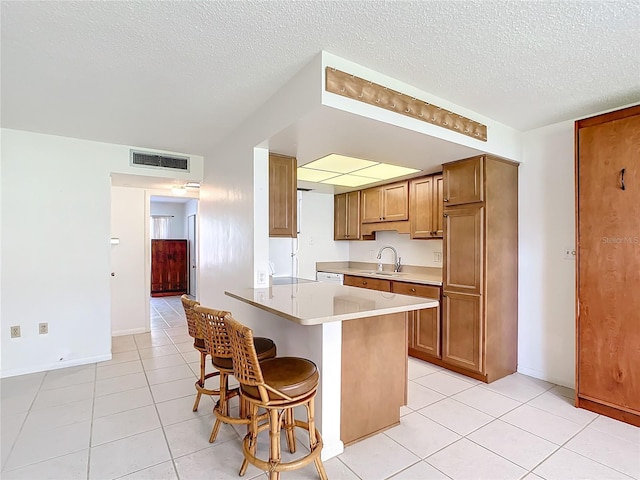 kitchen with brown cabinetry, a breakfast bar, visible vents, and a sink