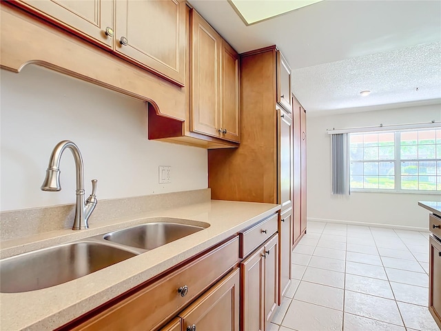 kitchen featuring a textured ceiling, light tile patterned floors, a sink, light countertops, and brown cabinetry