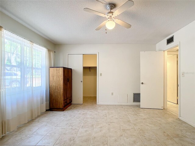 unfurnished bedroom featuring a textured ceiling, light tile patterned floors, a walk in closet, a closet, and ceiling fan