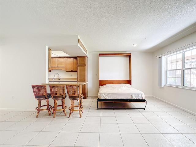 bedroom featuring a sink, a textured ceiling, baseboards, and light tile patterned floors