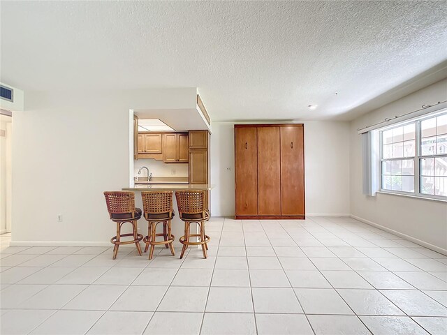 kitchen featuring light tile patterned flooring, sink, a kitchen bar, and kitchen peninsula