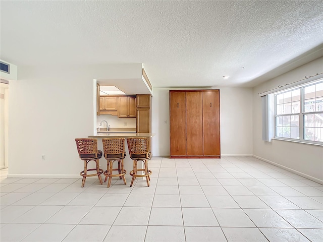 kitchen with brown cabinetry, a sink, a kitchen breakfast bar, a peninsula, and baseboards