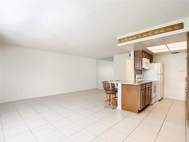 kitchen with a textured ceiling, a kitchen bar, white appliances, and light tile patterned floors