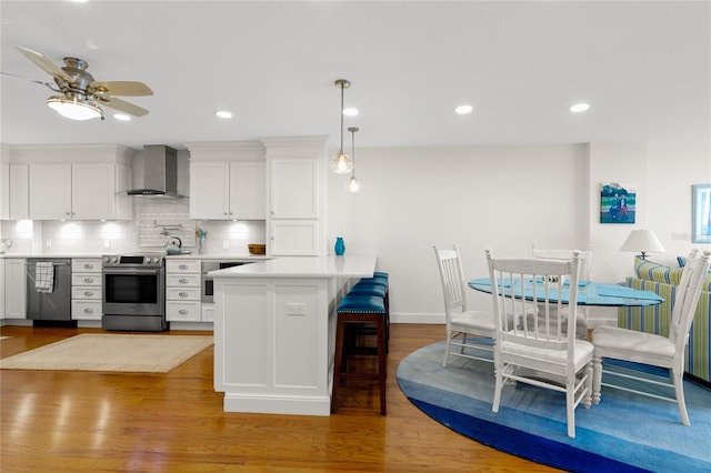 kitchen with backsplash, appliances with stainless steel finishes, wall chimney exhaust hood, white cabinetry, and hardwood / wood-style floors