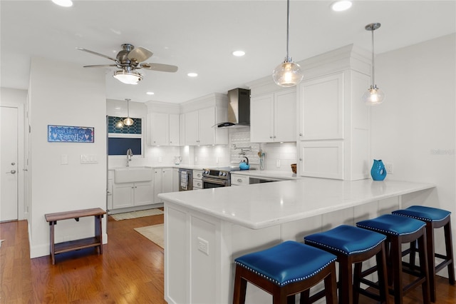 kitchen with kitchen peninsula, pendant lighting, wall chimney range hood, and a breakfast bar area