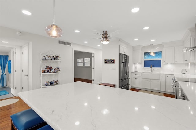 kitchen with appliances with stainless steel finishes, white cabinets, sink, light hardwood / wood-style floors, and hanging light fixtures