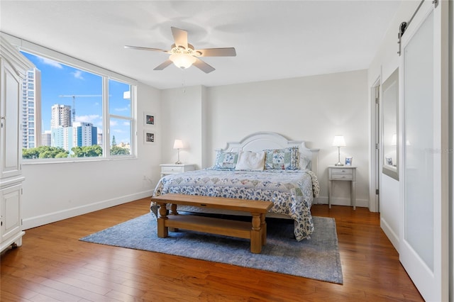 bedroom featuring a barn door, dark wood-type flooring, and ceiling fan