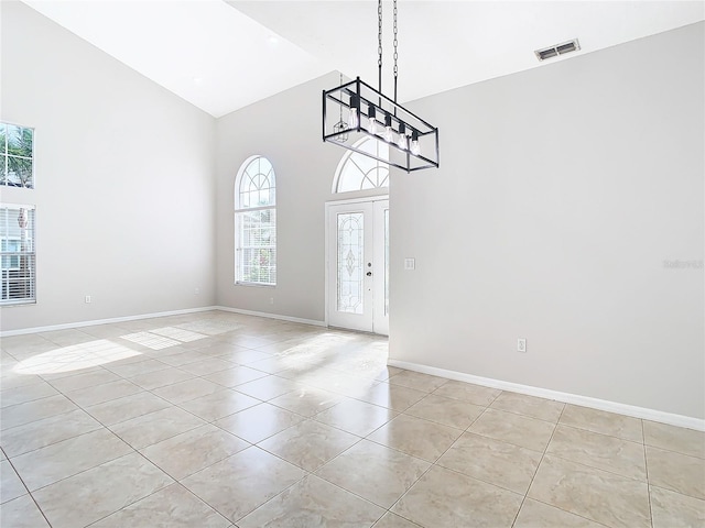 tiled empty room with high vaulted ceiling, plenty of natural light, and a chandelier