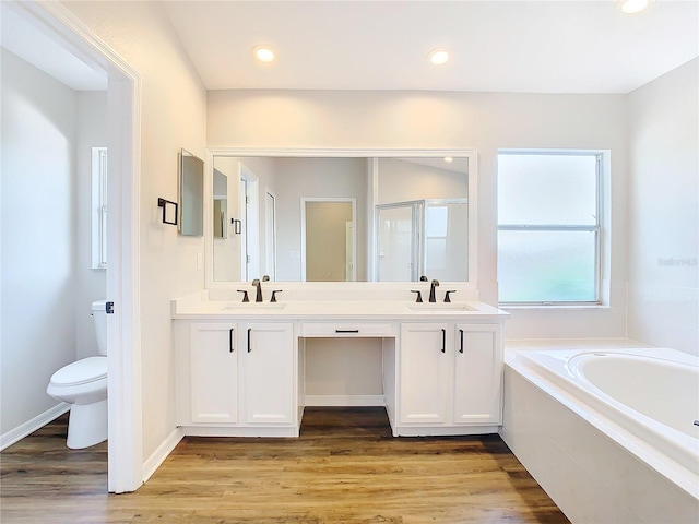 bathroom with dual sinks, tiled tub, oversized vanity, toilet, and hardwood / wood-style flooring