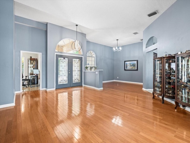 foyer with high vaulted ceiling, french doors, light hardwood / wood-style flooring, a notable chandelier, and a textured ceiling