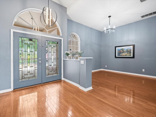 entryway featuring a notable chandelier, light hardwood / wood-style floors, french doors, and a towering ceiling