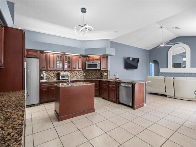 kitchen featuring a kitchen island with sink, hanging light fixtures, appliances with stainless steel finishes, vaulted ceiling, and tasteful backsplash