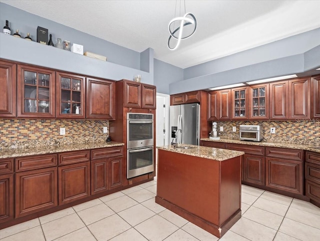 kitchen featuring decorative light fixtures, a kitchen island, backsplash, stainless steel appliances, and light stone counters