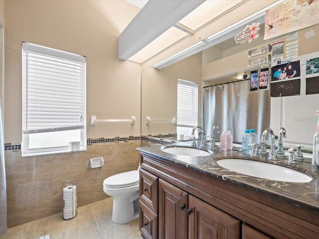 bathroom with vanity with extensive cabinet space, tile floors, tile walls, double sink, and toilet