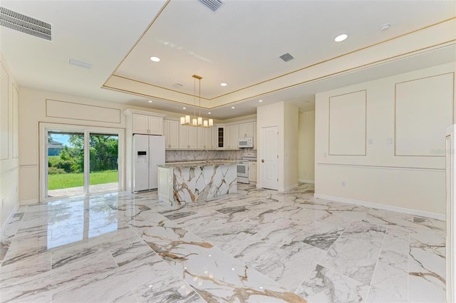 kitchen featuring a center island, tasteful backsplash, white appliances, pendant lighting, and a tray ceiling