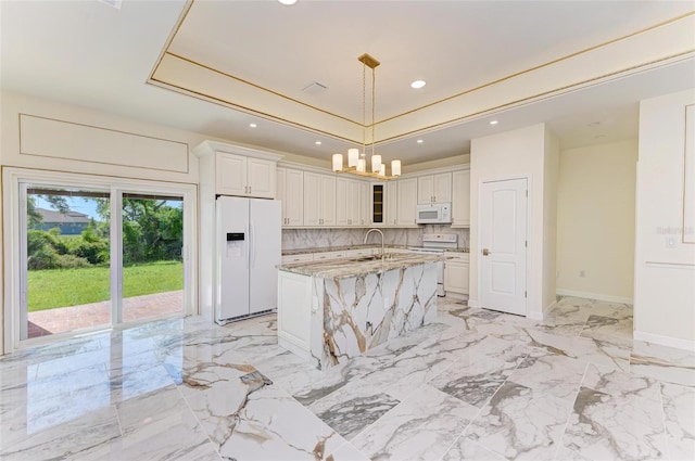 kitchen with light stone counters, white appliances, sink, a center island with sink, and decorative light fixtures