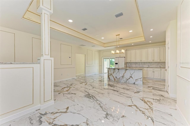 kitchen with cream cabinetry, a raised ceiling, white fridge with ice dispenser, light stone counters, and hanging light fixtures