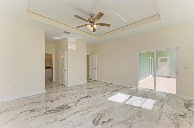 empty room with ceiling fan and a tray ceiling