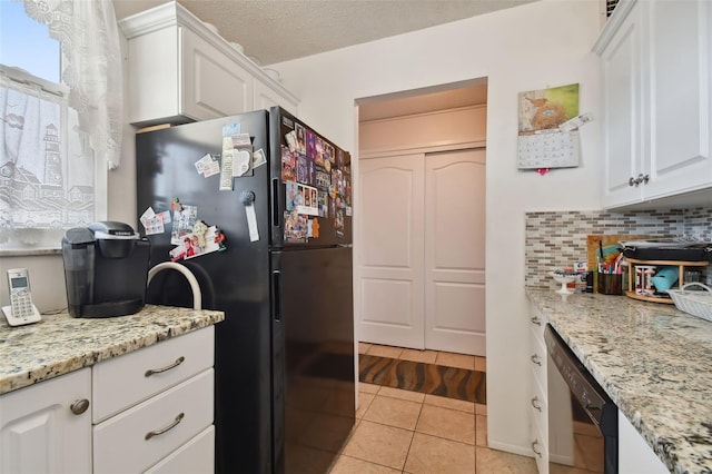 kitchen with black refrigerator, white cabinets, light tile floors, dishwasher, and backsplash