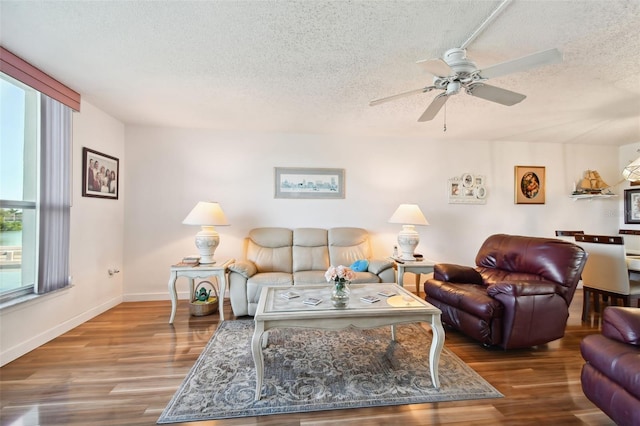 living room featuring ceiling fan, a textured ceiling, and dark wood-type flooring