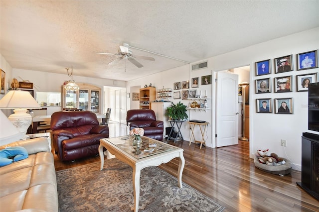 living room featuring ceiling fan, dark wood-type flooring, and a textured ceiling