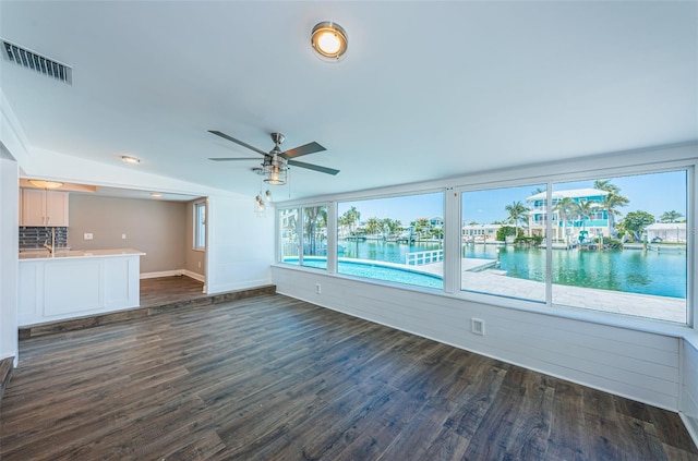 unfurnished living room featuring ceiling fan, dark hardwood / wood-style flooring, and a water view