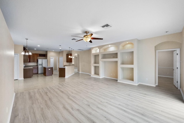 unfurnished living room featuring built in shelves, light hardwood / wood-style floors, and ceiling fan with notable chandelier