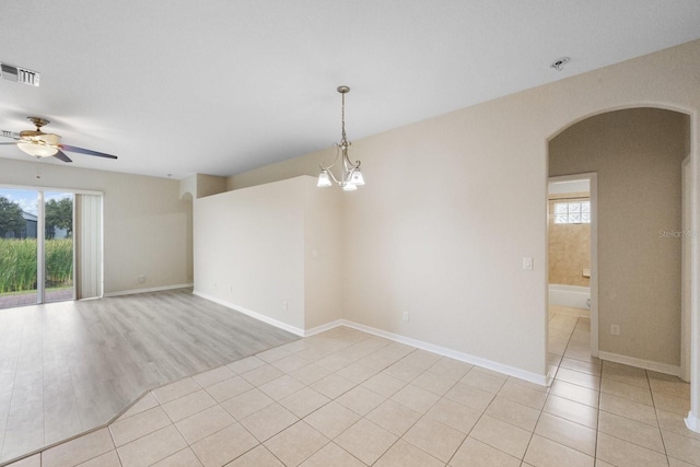 tiled empty room featuring ceiling fan with notable chandelier and a wealth of natural light