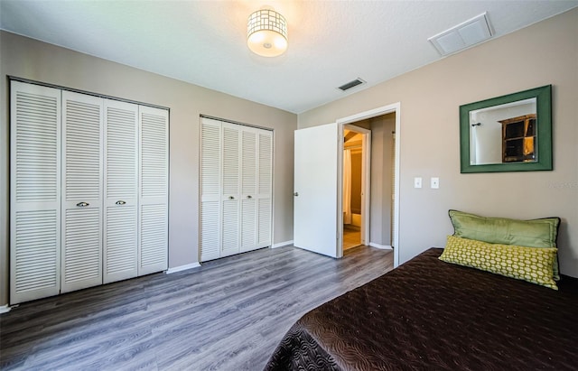 bedroom with multiple closets and dark wood-type flooring