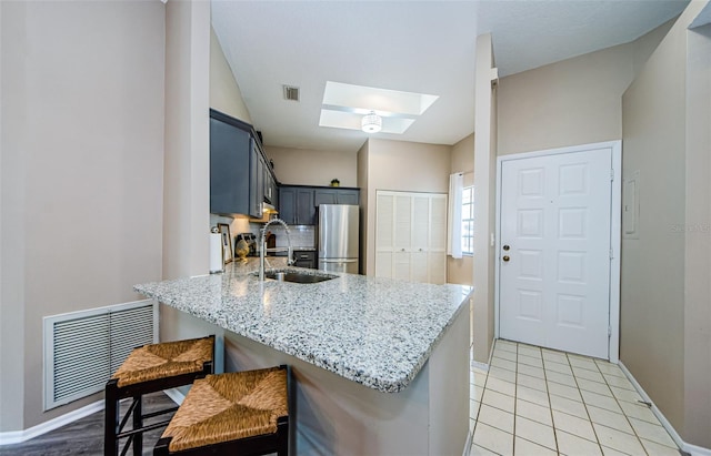 kitchen with kitchen peninsula, stainless steel fridge, sink, and a skylight