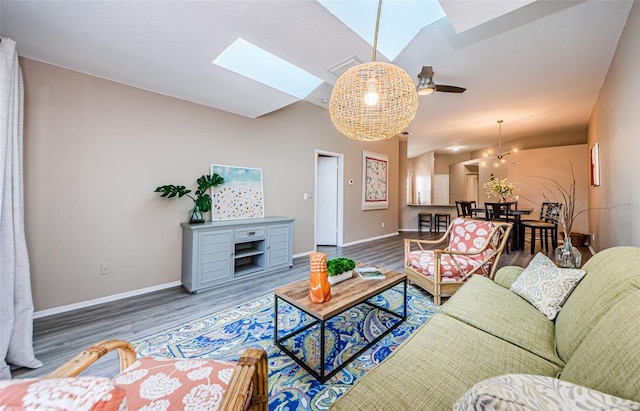 living room with ceiling fan, wood-type flooring, and lofted ceiling with skylight