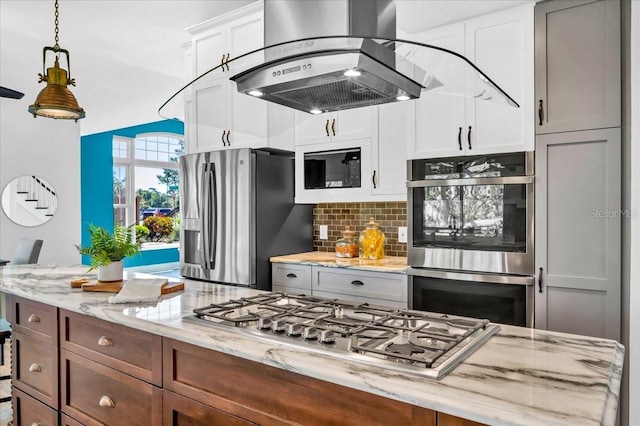 kitchen with decorative backsplash, light stone counters, white cabinetry, island range hood, and stainless steel appliances